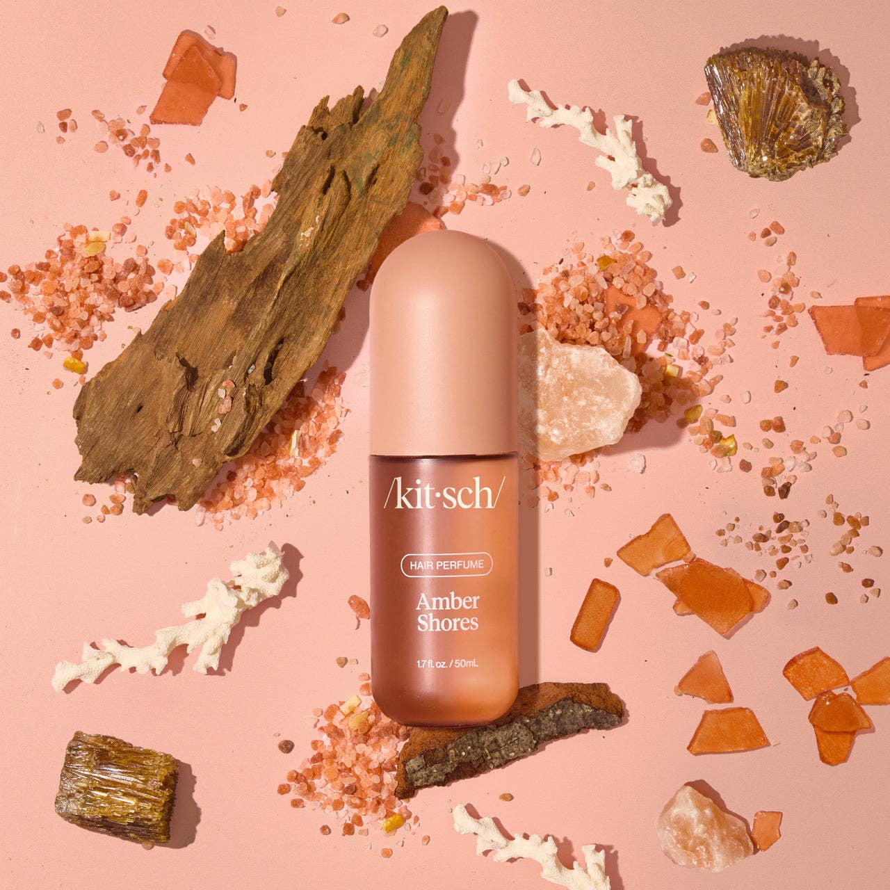 Amber Shores Hair Perfume bottle with pink cap on pink backdrop, surrounded by amber, driftwood, and sea salt crystals.